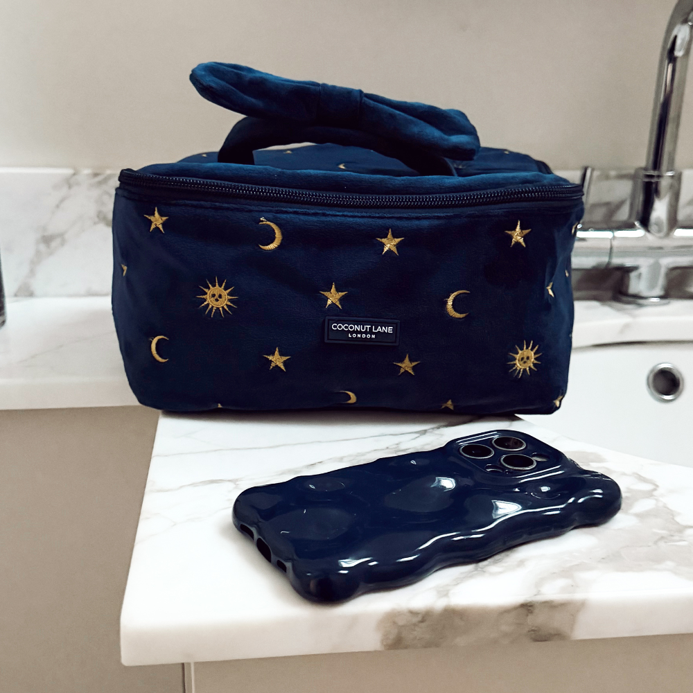 Coconut Lane Celestial travel vanity case with star pattern next to a dark blue phone on a white bathroom counter.