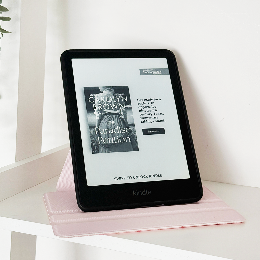 Pink Kindle case with ditsy floral pattern by Coconut Lane, holding a Kindle displaying Paradise Petition.