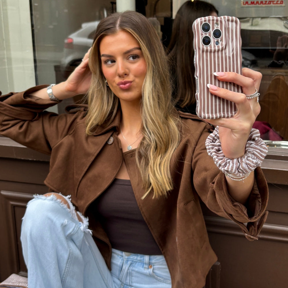 Woman in a brown jacket taking a mirror selfie with a phone in a chestnut striped Coconut Lane case.