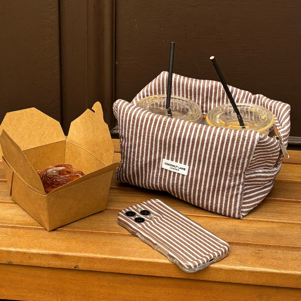 Chestnut striped wavy phone case next to a fabric drink carrier and takeout box on a wooden surface.