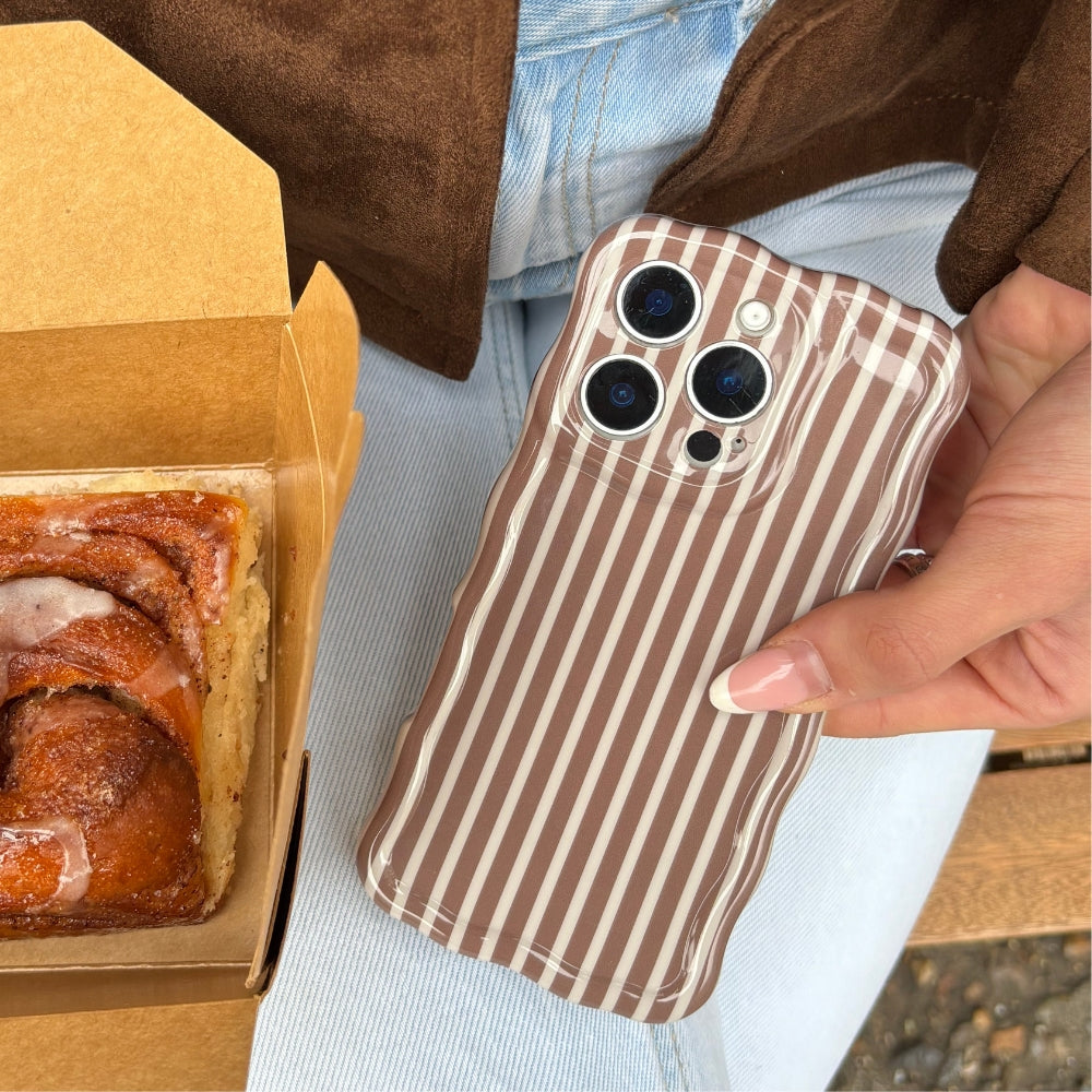 Hand holding chestnut striped wavy phone case near pastry in a box; person is wearing blue jeans.