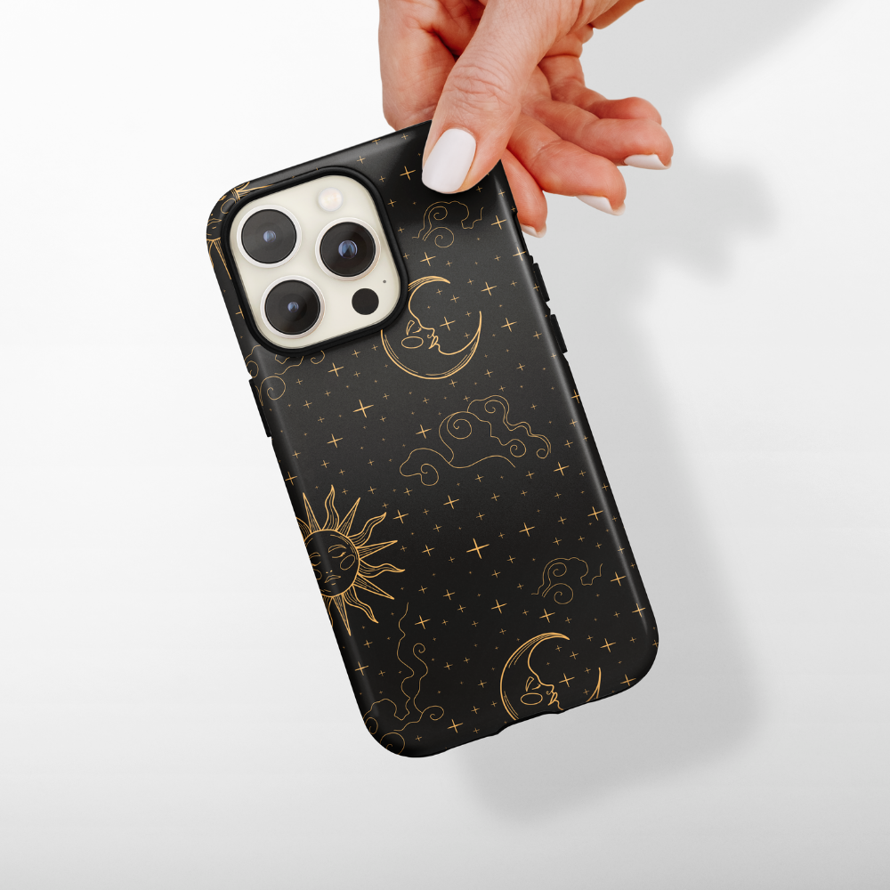 Hand holding a Coconut Lane Tough Phone Case with gold sun, moon, and stars pattern on a dark background.