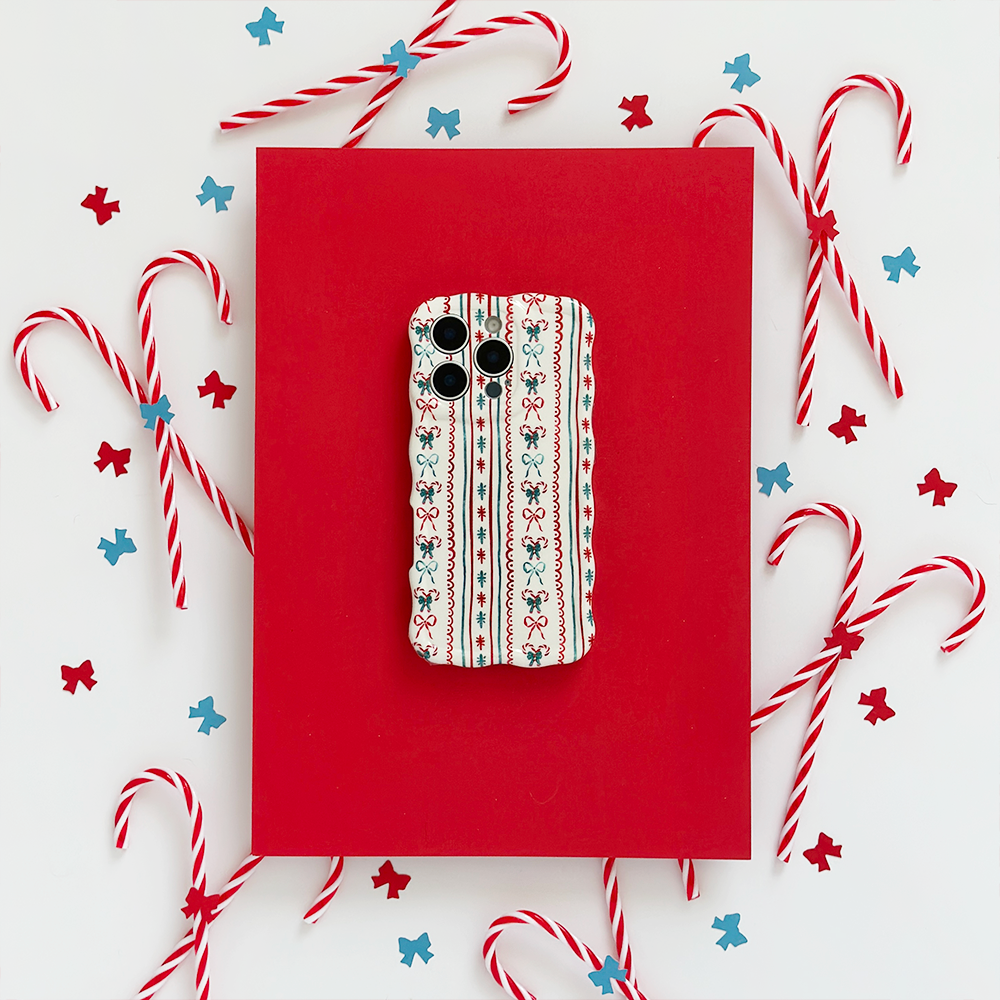 A smartphone with a festive patterned case is placed on a red rectangular surface, surrounded by candy canes and small red and blue star decorations on a white background.