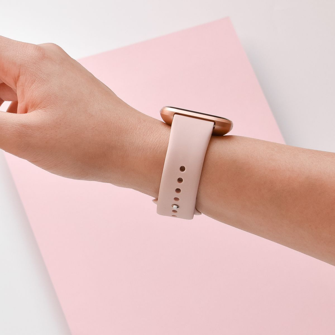 A close-up of a person's wrist wearing a smartwatch with a light pink band, set against a pink background.