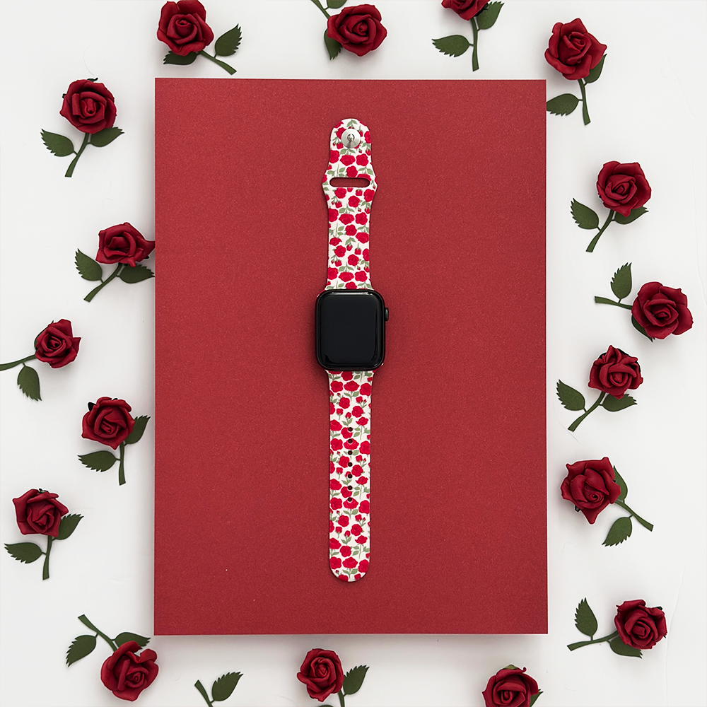 A smartwatch with a floral band is centered on a red rectangular background, surrounded by decorative red roses arranged in a symmetrical pattern.