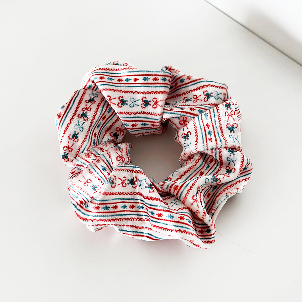 A scrunchie with a white base and red, green, and blue geometric and floral patterns rests on a white surface.