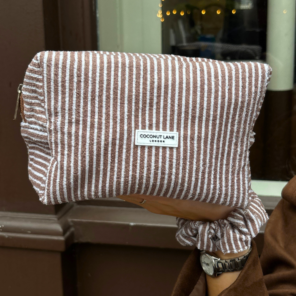 Striped pouch with a visible brand label held by a person wearing a brown coat.