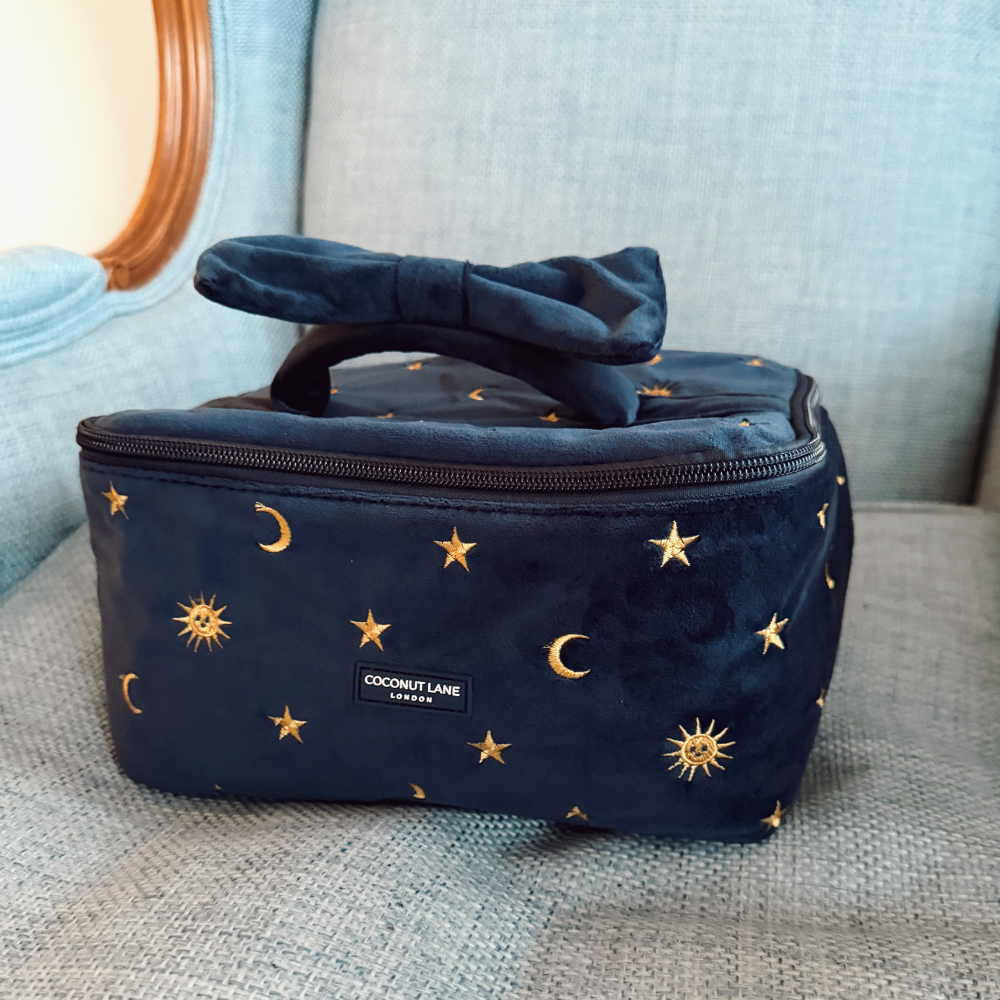 Navy blue velvet travel vanity case with gold moons and stars pattern, placed on a blue couch.