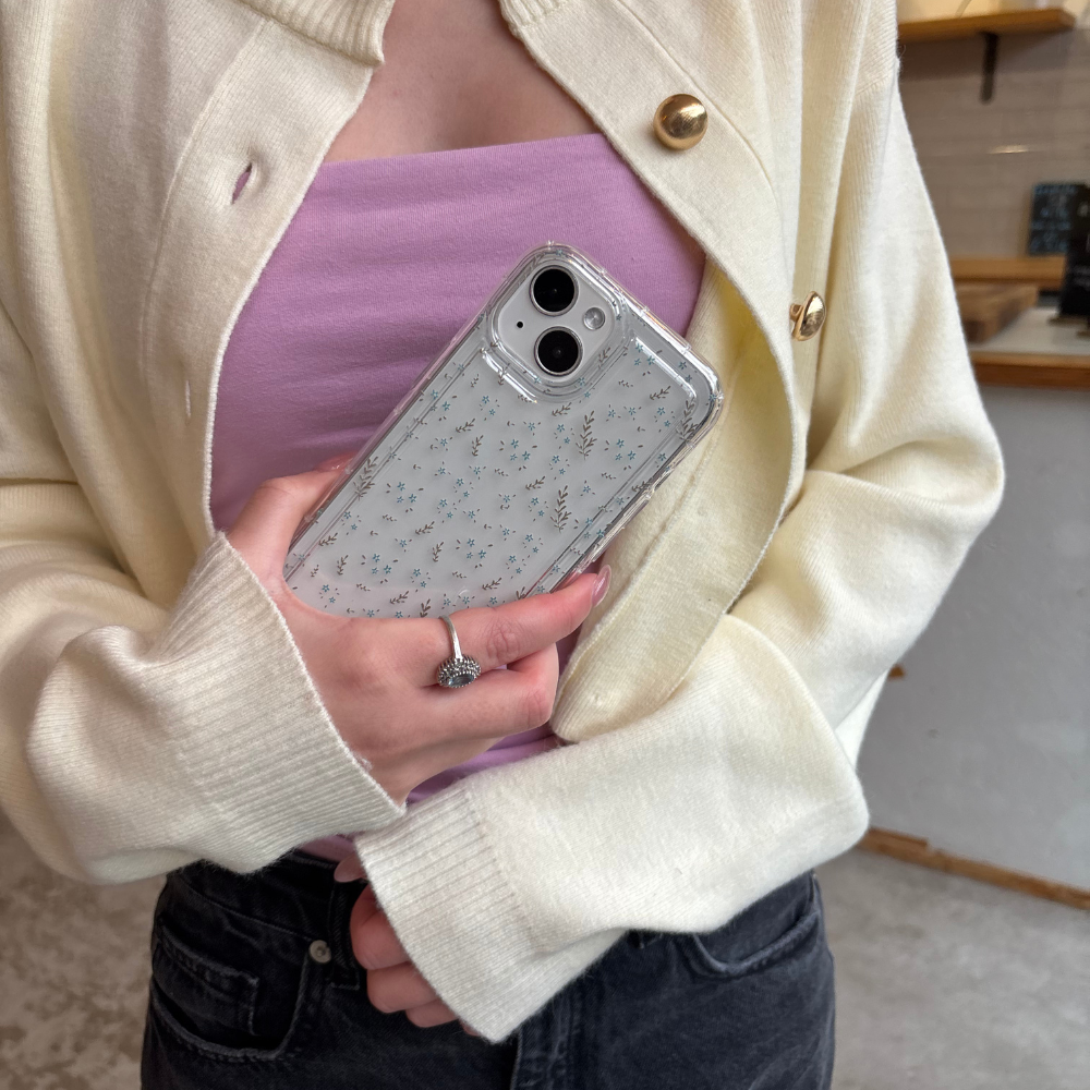 Hand holding Coconut Lane clear phone case with blue floral design, person wearing a cream cardigan.