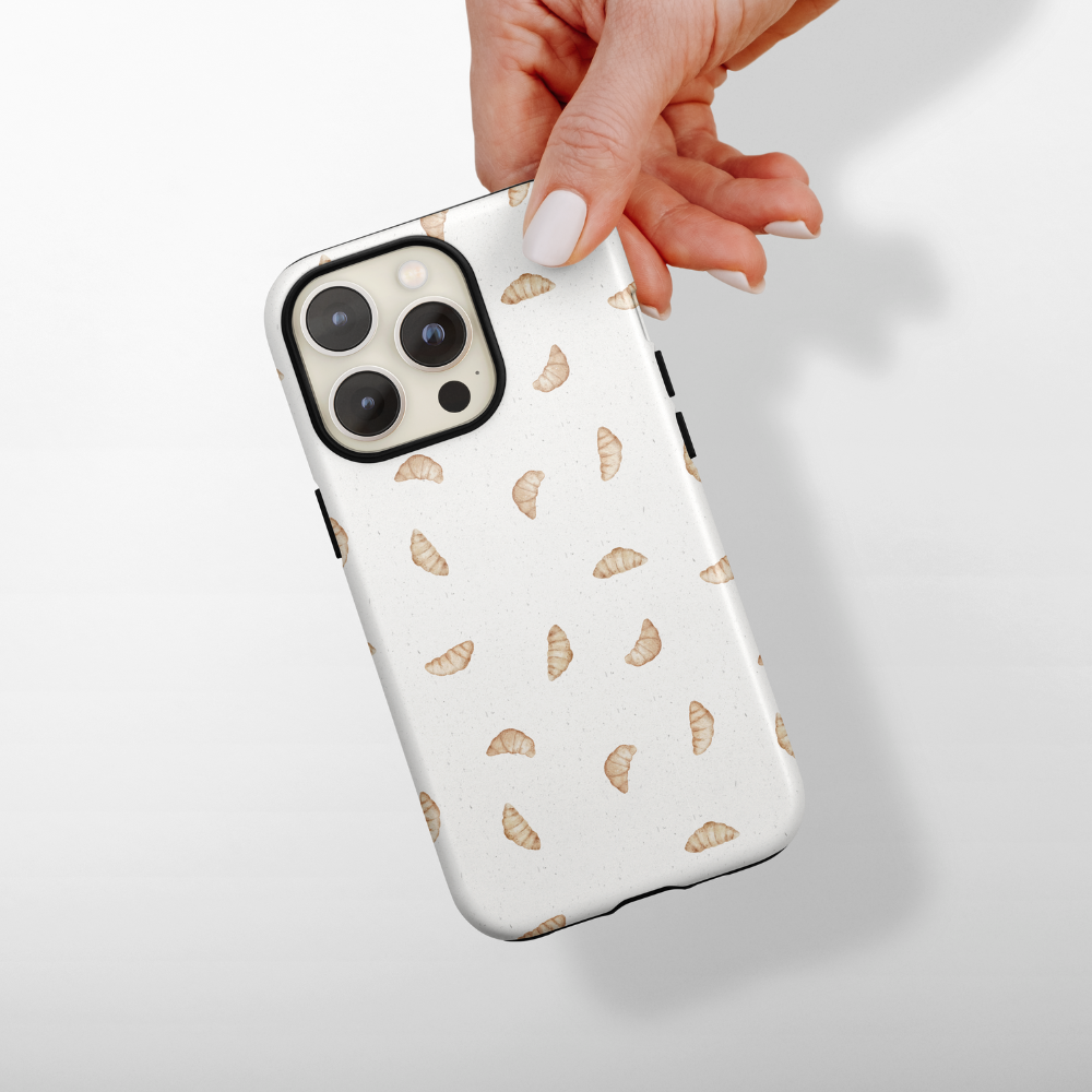 Hand holding an iPhone in a Coconut Lane Tough Phone Case with a playful croissant pattern.