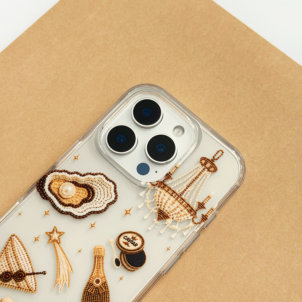 A clear phone case decorated with macron-style graphics of oysters, a cocktail, a champagne bottle, playing cards, and a macaron.