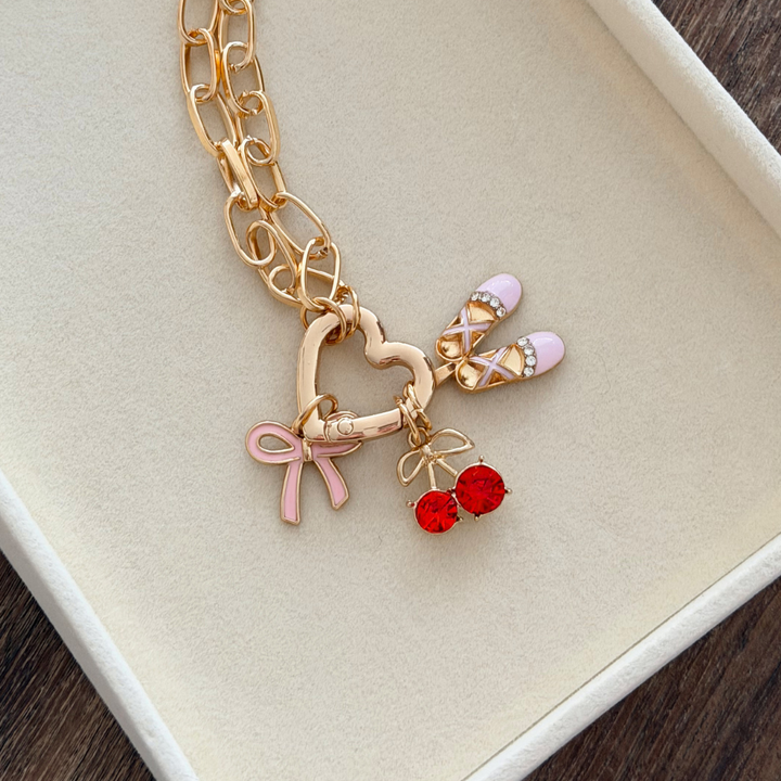 Gold Phone Strap with heart-shaped clasp and various charms on a beige background