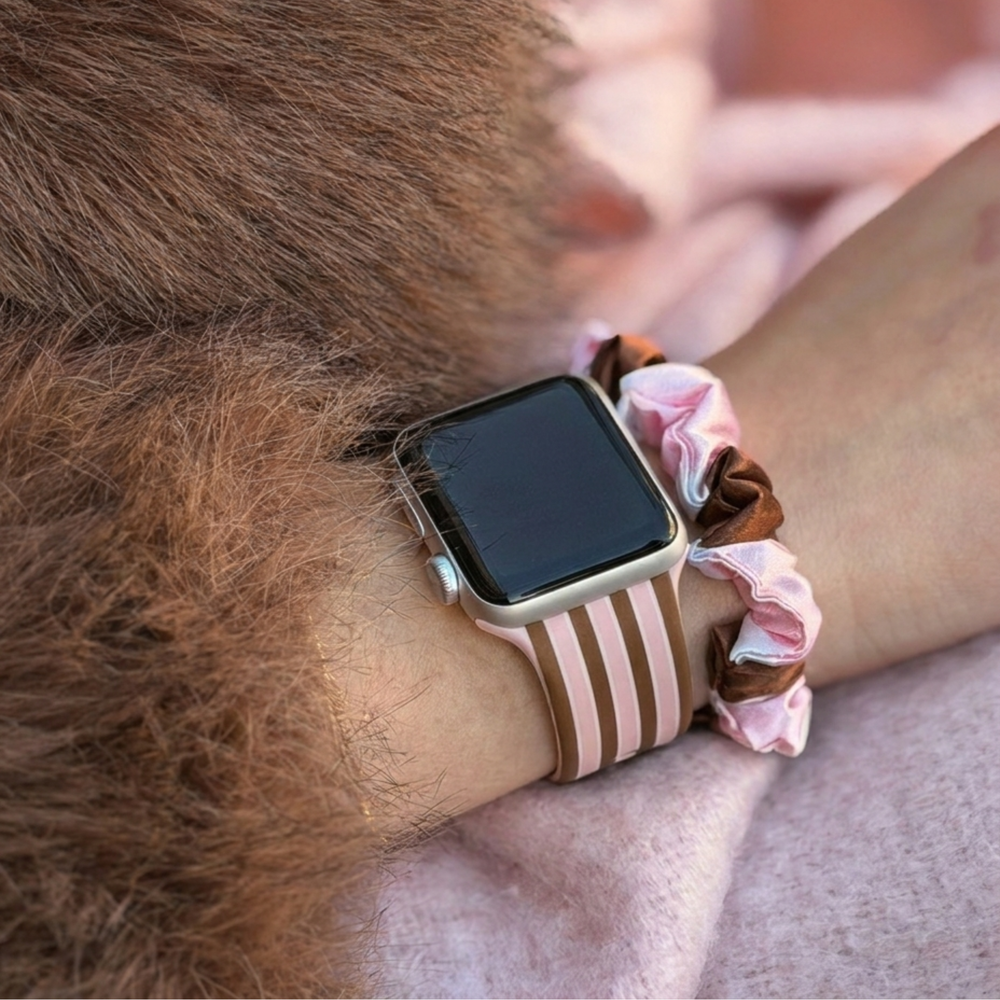 Pink and Brown stripes silicone sport band, attached to a black Apple Watch smartwatch on a woman's wrist alongside a matching cocoa and pink striped satin scrunchie.