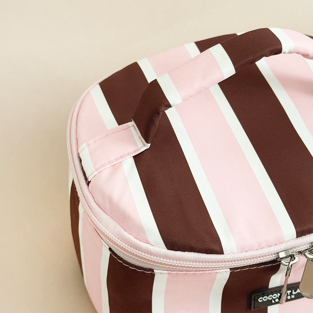 Close-up of Coconut Lane Cocoa & Pink Stripe round vanity case showing the matching striped carry handle, pink zip and fabric detailing.