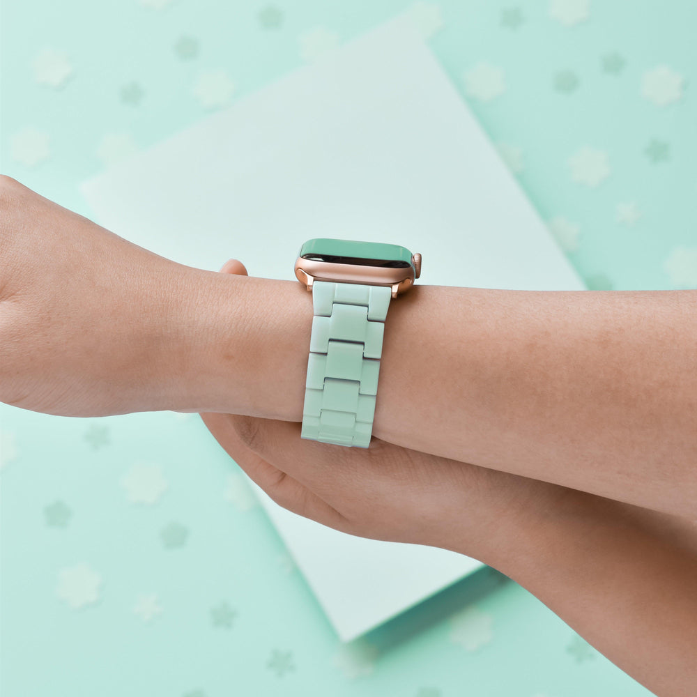 A person's wrist adorned with a Coconut Lane Luxe Pastel Mint Apple Watch Strap. The mint green background, accented by a subtle pattern of small, scattered shapes, complements the adjustable strap perfectly.