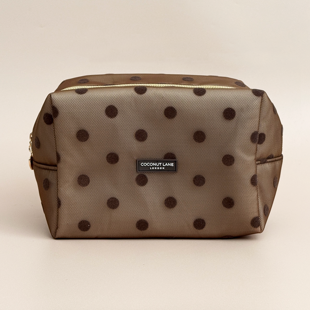 Brown mesh makeup bag with dark brown polka dots, a gold top zip with a heart-shaped zip pull, and a black Coconut Lane London logo badge on the front, shown on a beige background.