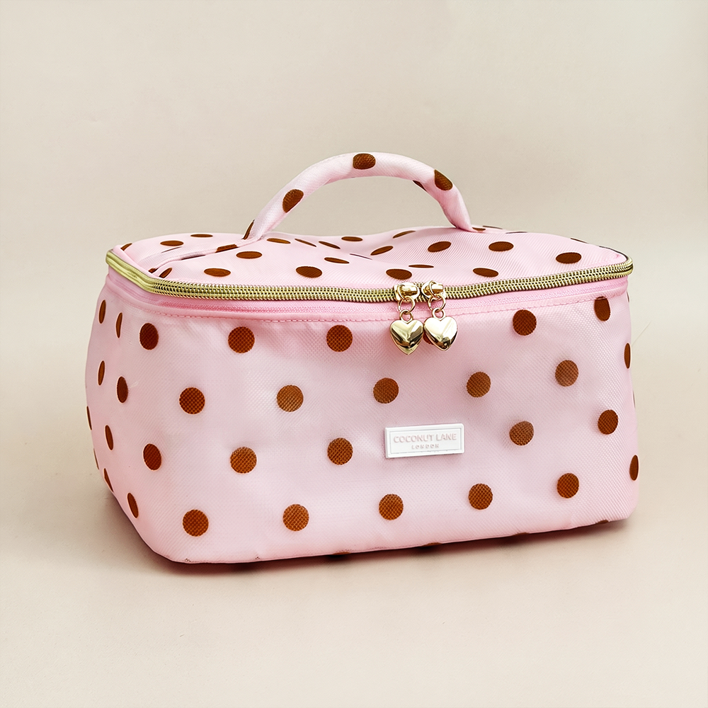 Pink mesh vanity case with brown polka dots, a padded polka dot top handle, gold zip with two heart-shaped zip pulls, and a white Coconut Lane London logo badge on the front, shown on a beige background.