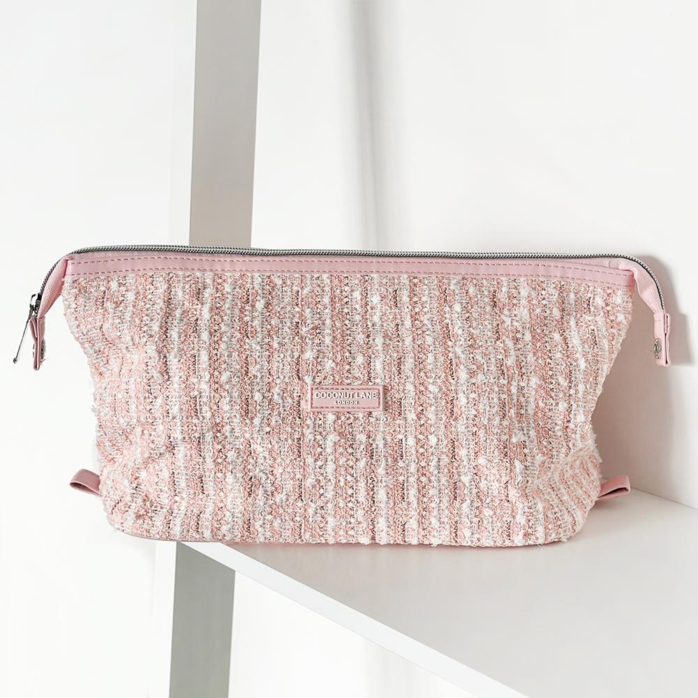 Pink textured tweed expandable makeup bag by Coconut Lane resting on a white shelf against a white background.