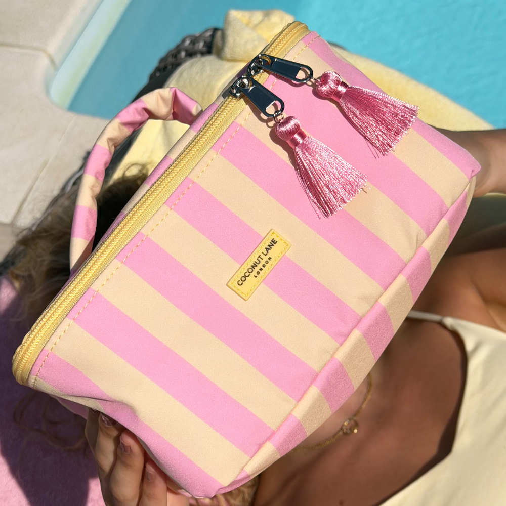 Pink and yellow striped vanity case with a tassel held by a girl by pool
