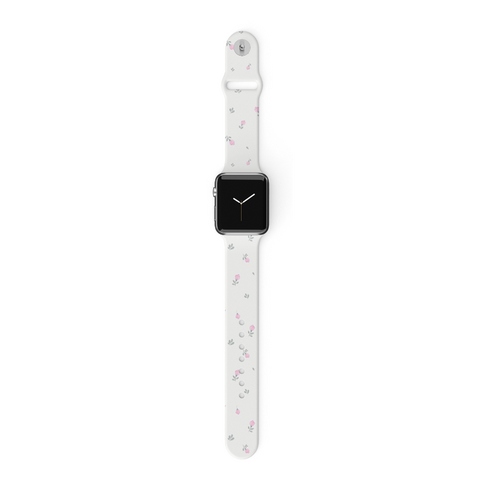 A white smartwatch with a rectangular face and black screen displaying the time is shown. The Ditsy Floral White Apple Watch Strap by Coconut Lane adds a touch of elegance, featuring small pink and gray flowers scattered on it. The watch is laid out flat against a plain white background.