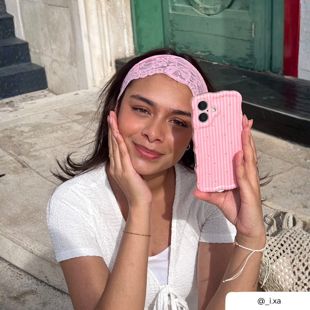 Girl with brunette hair wearing a pink lace hair band on her head, holding a wavy pink striped phone case with small spicy margarita illustrations.