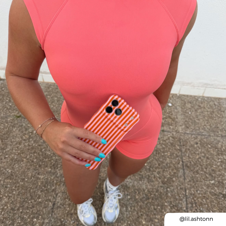 a woman wearing bright orange gym wear, holding an iphone, with a pink and orange striped phone case 