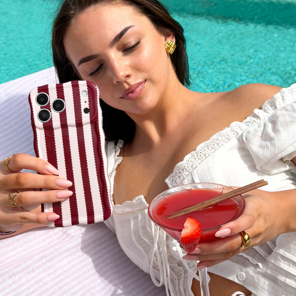 Girl sipping cocktail by the pool holding Wavy Blushberry Scallop Stripes Phone Case