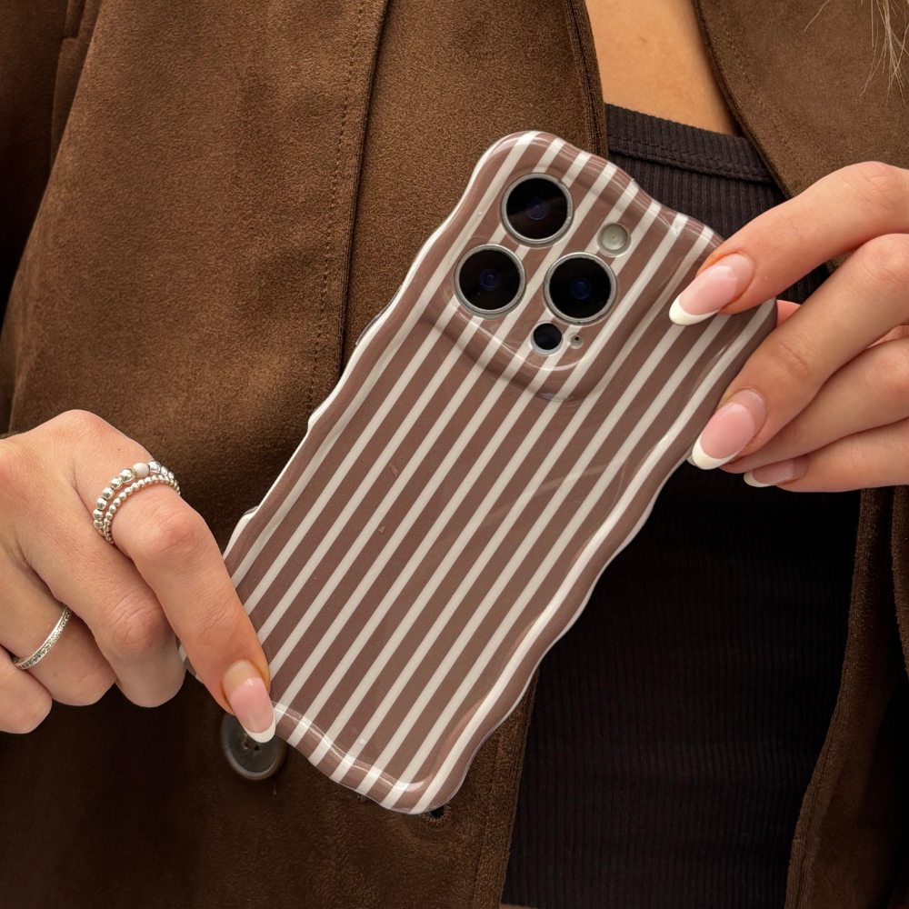 Hand holding a Coconut Lane phone case with chestnut wavy stripes, brown jacket and rings visible.