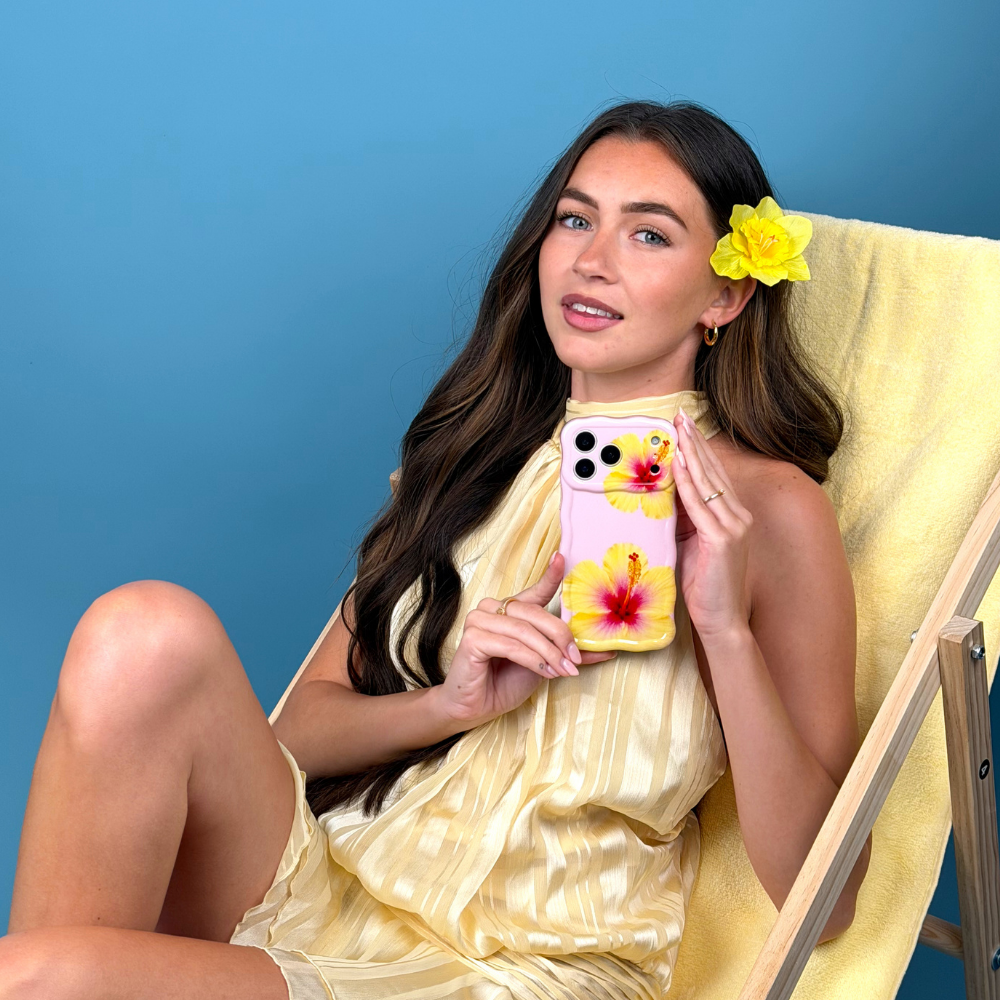 Woman in a yellow dress with a floral phone case sitting on a yellow chair against a blue background