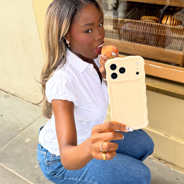 Girl crouching eating a peach holding her wavy milky peach phone case