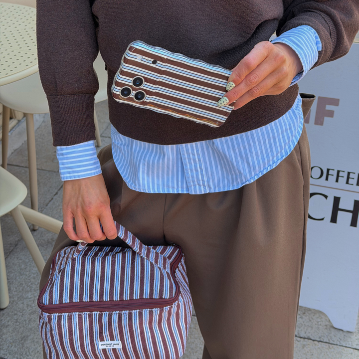 Girl in cafe holding Wavy Brown and Blue Stripes Phone Case in matching outfit holding vanity case