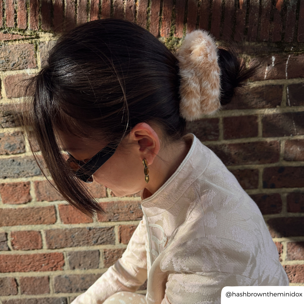 girl with dark hair wearing sunglasses, her hair is in a bun with a fluffy fawn material scrunchie in it