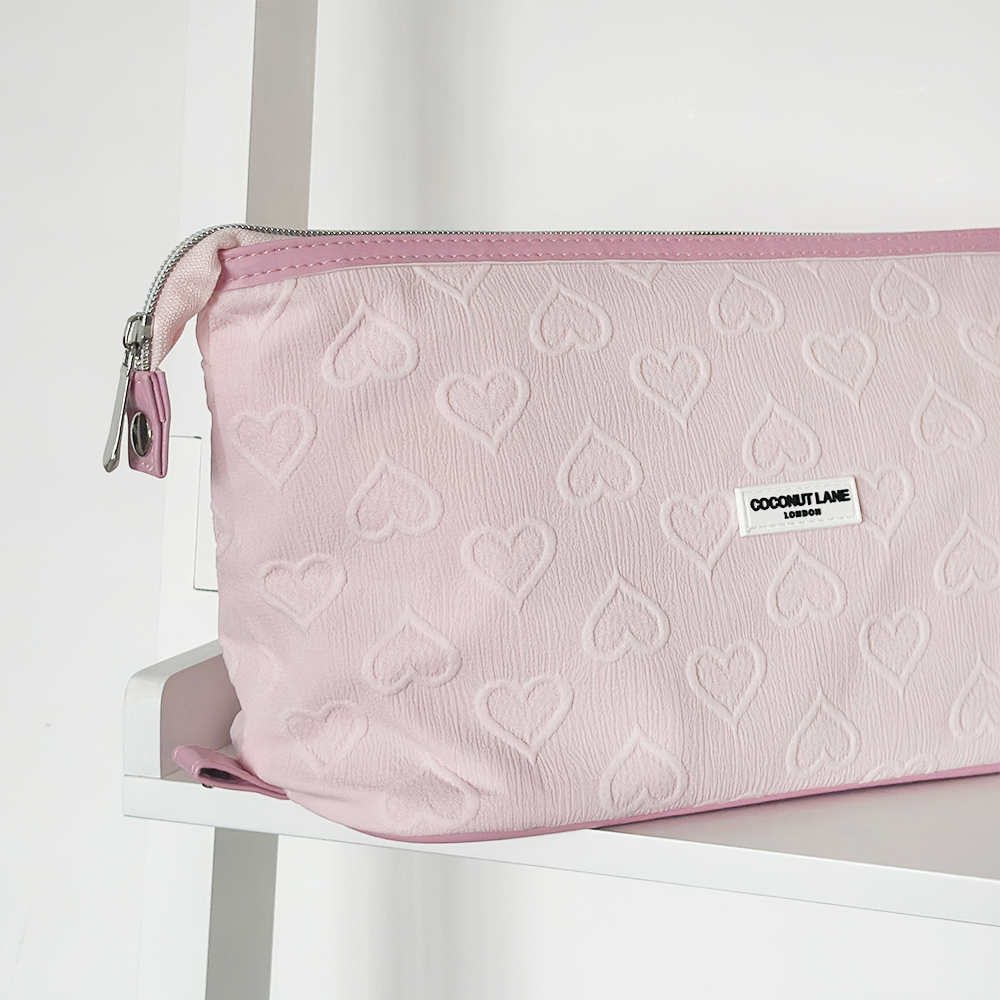 Baby pink expandable makeup bag with embossed heart pattern, displayed on a white shelf.