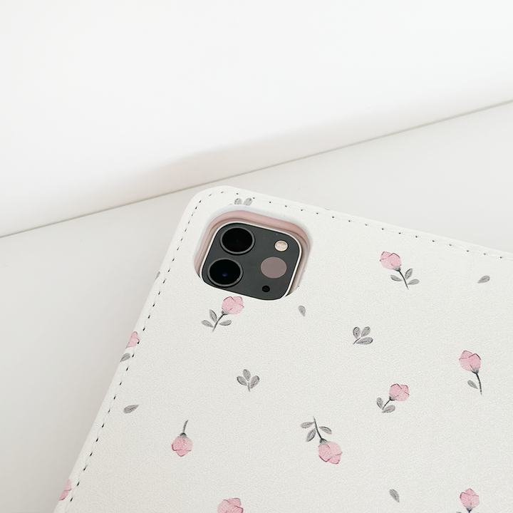 A close-up of an iPad featuring the Ditsy Floral White iPad Case by Coconut Lane. The pristine white case, adorned with small pink flowers and green leaves, includes anti-slip features for a better grip. The device's camera is visible in the upper left corner, set against a pristine white background.